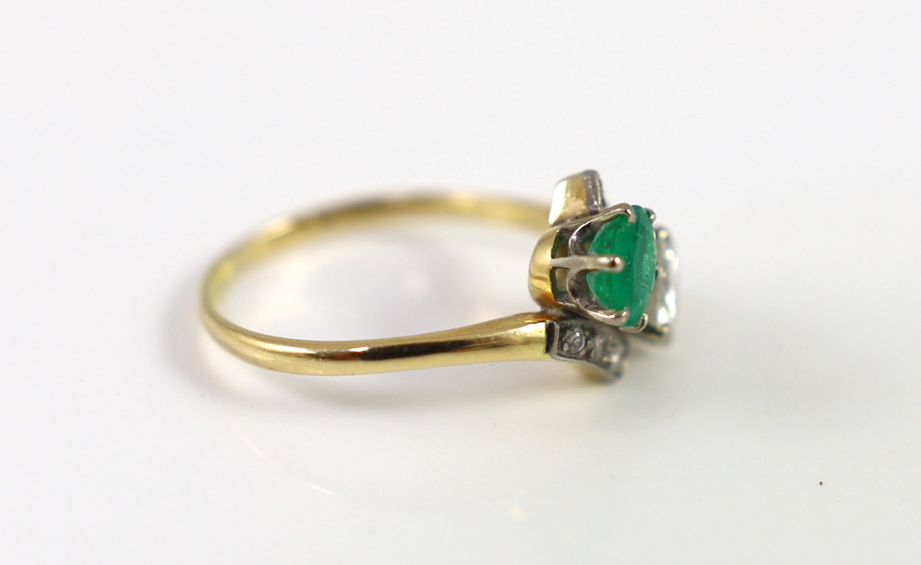 A gold, emerald and diamond set two stone cross-over ring, with diamond set shoulders